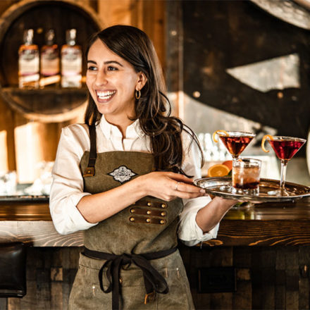 A happy server at Fremont Mischief Distillery holding a tray of drinks.